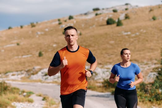 A couple dressed in sportswear runs along a scenic road during an early morning workout, enjoying the fresh air and maintaining a healthy lifestyle.