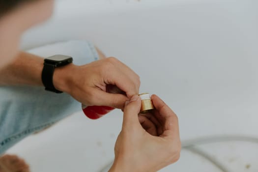 One young Caucasian unrecognizable guy wraps white tow on the nut of a faucet while sitting in the bathroom at home, close-up side view.Step by step.