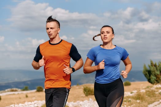 A couple dressed in sportswear runs along a scenic road during an early morning workout, enjoying the fresh air and maintaining a healthy lifestyle.