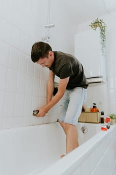 One young brunette Caucasian man tightens the faucet nut with both hands using an adjustable wrench in the bathroom sticking out of the wall, standing in the bathroom during the day, close-up side view.Step by step.