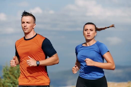 A couple dressed in sportswear runs along a scenic road during an early morning workout, enjoying the fresh air and maintaining a healthy lifestyle.