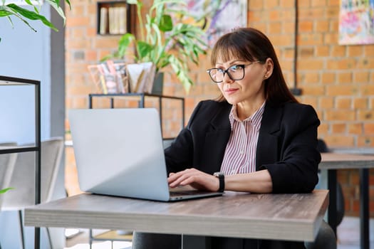 Middle-aged business confident successful serious woman working remotely at table with laptop computer in coworking cafe. Business, mature people, success, leadership, management, empowerment concept