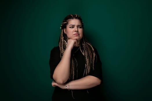 A woman with dreadlocks is standing in front of a bright green wall. She is looking directly at the camera with a confident expression. The womans hair is styled in thick, long dreadlocks that cascade down her back. Her outfit is casual and she appears to be outdoors.