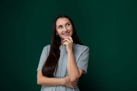 A woman with long hair is standing in front of a vibrant green wall, looking directly at the camera. She appears confident and serene in her stance.