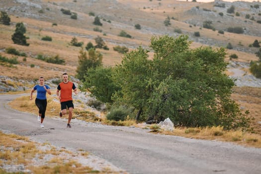 A couple dressed in sportswear runs along a scenic road during an early morning workout, enjoying the fresh air and maintaining a healthy lifestyle.