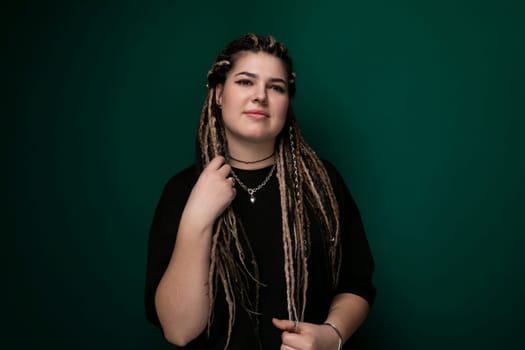 A woman with dreadlocks is shown standing in front of a solid green background. She is wearing casual clothing and has a relaxed posture. The focus is on her unique hairstyle and the contrast against the vibrant green backdrop.