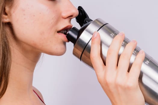 Closeup side view of a sportive female after training who drinking fresh water from sport bottle