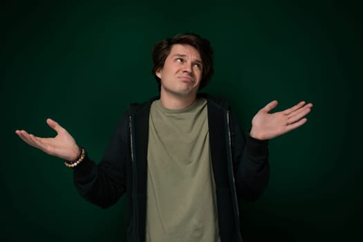 A man is standing in front of a bright green wall with his hands stretched out in front of him. He appears to be either gesturing or expressing something with his body language.