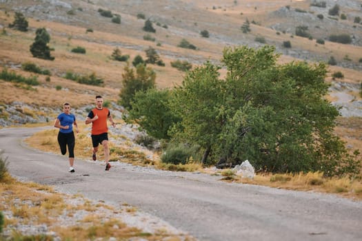 A couple dressed in sportswear runs along a scenic road during an early morning workout, enjoying the fresh air and maintaining a healthy lifestyle.