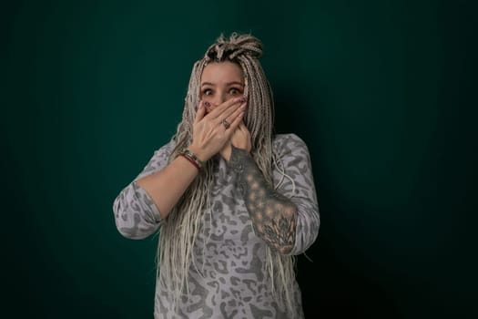 A woman is shown covering her mouth with both hands. Her facial expression suggests shock, surprise, or horror. The action conveys a sense of secrecy or suppression.