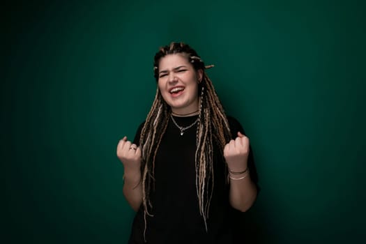 A woman with dreadlocks is standing in front of a bright green wall. She is looking directly at the camera with a confident expression, her hair falling loosely around her shoulders.