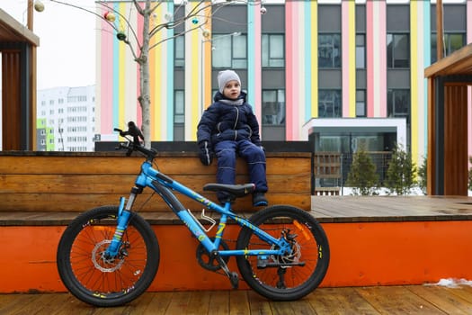 A European boy dressed in a winter jacket gets off his bike.