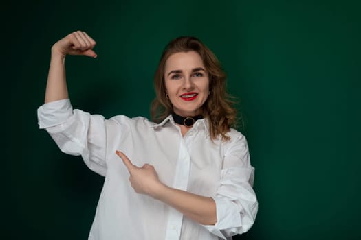 A woman in a white shirt confidently poses for a photograph, standing in a well-lit environment with a relaxed expression. She is striking a pose for the camera, showcasing her stylish outfit.