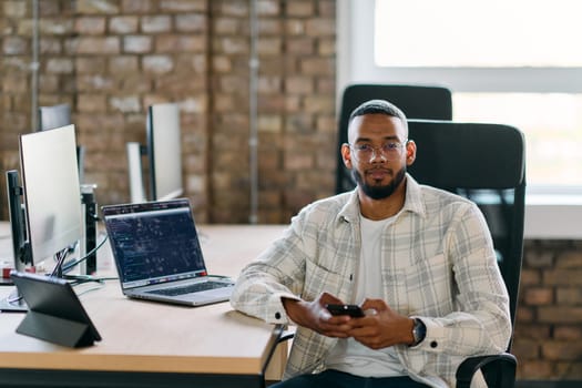 African American entrepreneur takes a break in a modern office, using a smartphone to browse social media, capturing a moment of digital connectivity and relaxation amidst his business endeavors