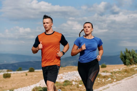 A couple dressed in sportswear runs along a scenic road during an early morning workout, enjoying the fresh air and maintaining a healthy lifestyle.