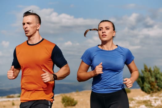 A couple dressed in sportswear runs along a scenic road during an early morning workout, enjoying the fresh air and maintaining a healthy lifestyle.