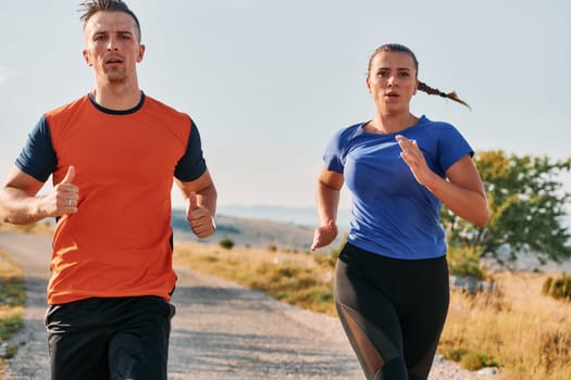 A couple dressed in sportswear runs along a scenic road during an early morning workout, enjoying the fresh air and maintaining a healthy lifestyle.