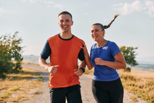 A couple dressed in sportswear runs along a scenic road during an early morning workout, enjoying the fresh air and maintaining a healthy lifestyle.