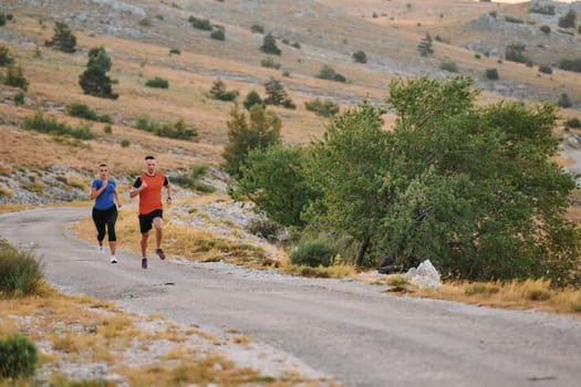 A couple dressed in sportswear runs along a scenic road during an early morning workout, enjoying the fresh air and maintaining a healthy lifestyle.