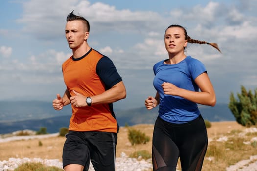 A couple dressed in sportswear runs along a scenic road during an early morning workout, enjoying the fresh air and maintaining a healthy lifestyle.