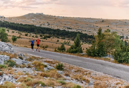 A couple dressed in sportswear runs along a scenic road during an early morning workout, enjoying the fresh air and maintaining a healthy lifestyle.