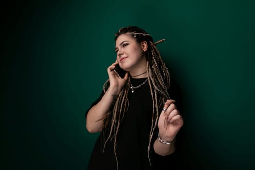 A woman with dreadlocks is engaged in a phone conversation while holding a cell phone to her ear. Her hair is styled in long, thin locks. She appears focused and attentive to the call as she stands.