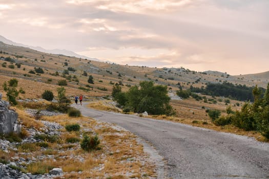 A couple dressed in sportswear runs along a scenic road during an early morning workout, enjoying the fresh air and maintaining a healthy lifestyle.