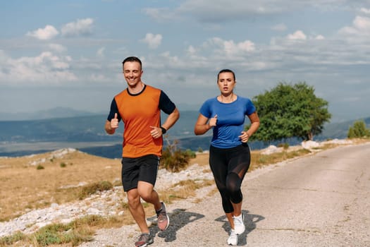 A couple dressed in sportswear runs along a scenic road during an early morning workout, enjoying the fresh air and maintaining a healthy lifestyle.