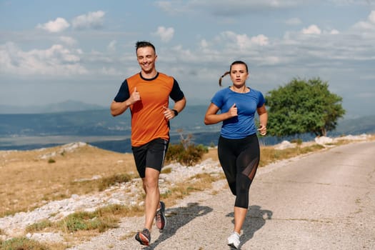 A couple dressed in sportswear runs along a scenic road during an early morning workout, enjoying the fresh air and maintaining a healthy lifestyle.