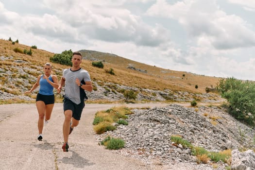 A couple dressed in sportswear runs along a scenic road during an early morning workout, enjoying the fresh air and maintaining a healthy lifestyle.