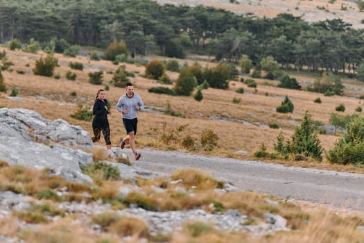 A couple dressed in sportswear runs along a scenic road during an early morning workout, enjoying the fresh air and maintaining a healthy lifestyle.