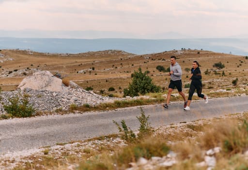 A couple dressed in sportswear runs along a scenic road during an early morning workout, enjoying the fresh air and maintaining a healthy lifestyle.