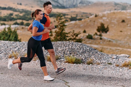 A couple dressed in sportswear runs along a scenic road during an early morning workout, enjoying the fresh air and maintaining a healthy lifestyle.