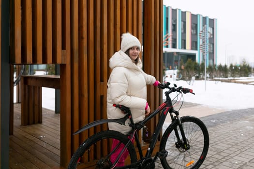 A woman is standing next to a bike parked in front of a building. She is looking at her phone, with a helmet in her hand.