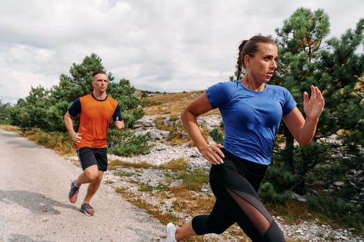 A couple dressed in sportswear runs along a scenic road during an early morning workout, enjoying the fresh air and maintaining a healthy lifestyle.