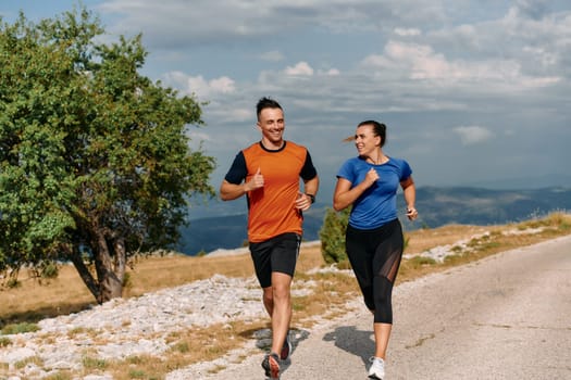 A couple dressed in sportswear runs along a scenic road during an early morning workout, enjoying the fresh air and maintaining a healthy lifestyle.