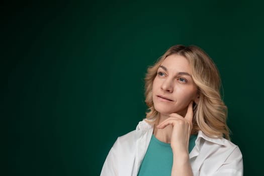 A woman standing in a confident pose, smiling for a picture in front of a solid green background. She is dressed in casual attire.