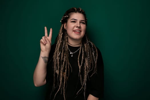 A woman with dreadlocks is shown raising her hand to make a peace sign gesture. She appears relaxed and confident in her gesture, showcasing a sense of unity and positivity.