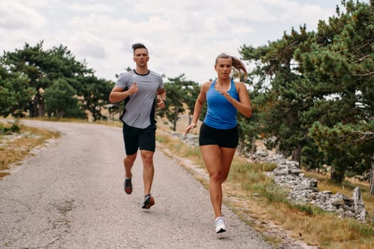 A couple dressed in sportswear runs along a scenic road during an early morning workout, enjoying the fresh air and maintaining a healthy lifestyle.