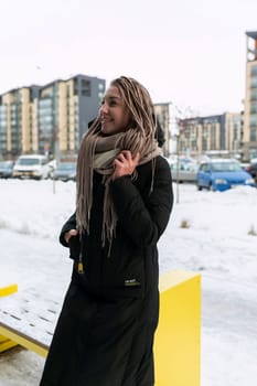 A pretty young woman with blond dreadlocks walks through the city in winter.