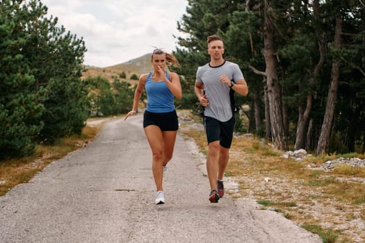 A couple dressed in sportswear runs along a scenic road during an early morning workout, enjoying the fresh air and maintaining a healthy lifestyle.