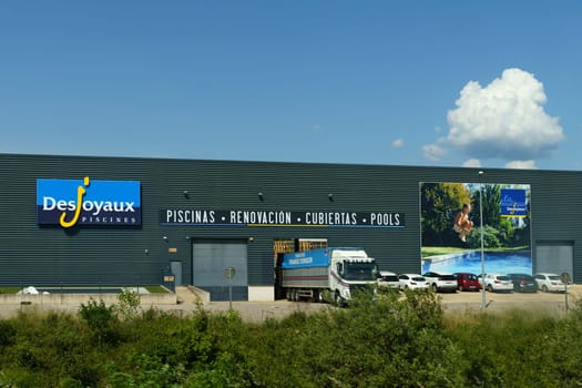 Barcelona, Spain - May 24, 2023: Trucks parked outside the Desjoyaux Pools showroom with a clear blue sky overhead, showcasing advertisements for swimming pools and renovations.