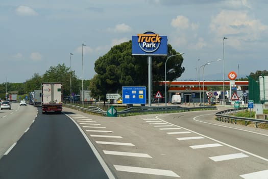 Barcelona, Spain - May 24, 2023: A truck is seen driving down a highway next to a gas station. The vehicle is moving, and the gas station is located on the side of the road. Truck park