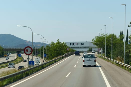Barcelona, Spain - May 24, 2023: A car drives on a highway past the Fujifilm factory, showcasing the buildings exterior under clear, blue skies.