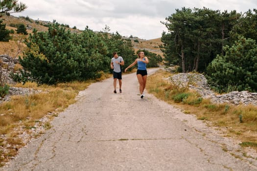 A couple dressed in sportswear runs along a scenic road during an early morning workout, enjoying the fresh air and maintaining a healthy lifestyle.