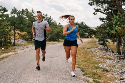 A couple dressed in sportswear runs along a scenic road during an early morning workout, enjoying the fresh air and maintaining a healthy lifestyle.