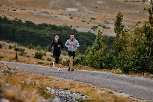 A couple dressed in sportswear runs along a scenic road during an early morning workout, enjoying the fresh air and maintaining a healthy lifestyle.