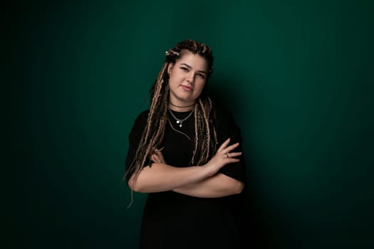 A woman with dreadlocks is standing confidently in front of a bright green wall. Her hair is styled in intricate dreadlocks, and she is wearing casual attire. The contrast between her dark hair and the vibrant wall creates a striking visual.