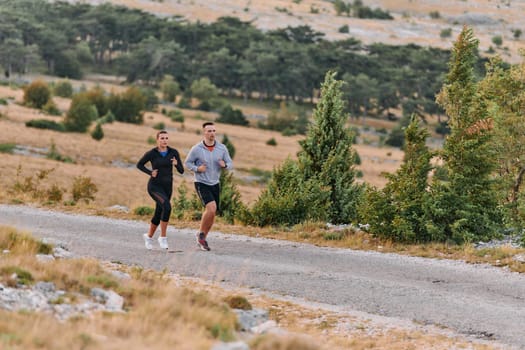 A couple dressed in sportswear runs along a scenic road during an early morning workout, enjoying the fresh air and maintaining a healthy lifestyle.