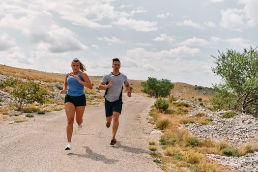 A couple dressed in sportswear runs along a scenic road during an early morning workout, enjoying the fresh air and maintaining a healthy lifestyle.